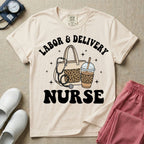 A Labor and Delivery nurse graphic featuring a large beige tote bag with a leopard print pocket, a stethoscope draped over it, and a large iced coffee cup with a matching leopard print sleeve, all surrounded by white text that reads LABOR & DELIVERY curved above and NURSE below.