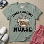 A Labor and Delivery nurse graphic featuring a large beige tote bag with a leopard print pocket, a stethoscope draped over it, and a large iced coffee cup with a matching leopard print sleeve, all surrounded by white text that reads LABOR & DELIVERY curved above and NURSE below.