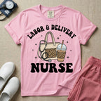 A Labor and Delivery nurse graphic featuring a large beige tote bag with a leopard print pocket, a stethoscope draped over it, and a large iced coffee cup with a matching leopard print sleeve, all surrounded by white text that reads LABOR & DELIVERY curved above and NURSE below.