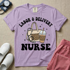 A Labor and Delivery nurse graphic featuring a large beige tote bag with a leopard print pocket, a stethoscope draped over it, and a large iced coffee cup with a matching leopard print sleeve, all surrounded by white text that reads LABOR & DELIVERY curved above and NURSE below.