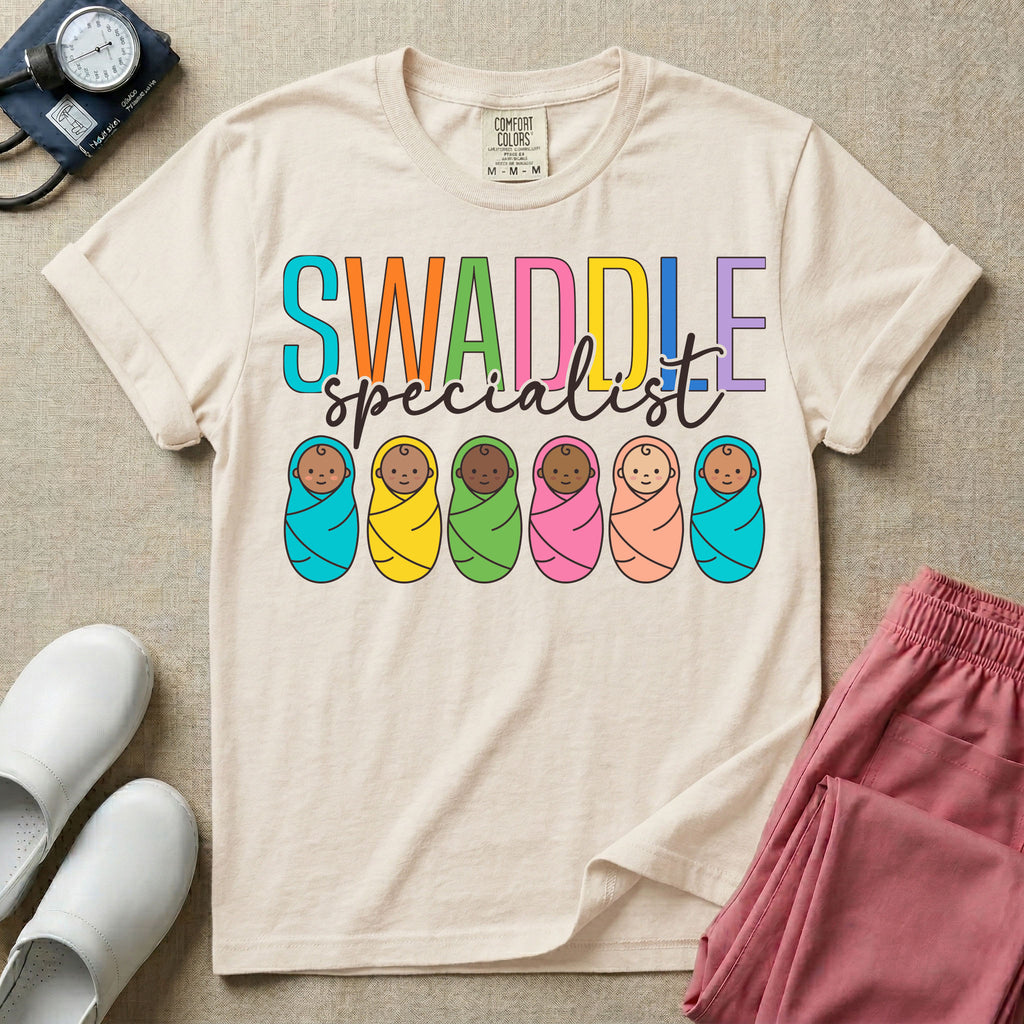 A cute neonatal and postpartum nurse graphic featuring the word SWADDLE in bright multicolored block letters above the word specialist in a white cursive font, positioned over a row of six diverse babies wrapped in brightly colored swaddles.