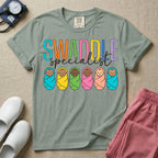 A cute neonatal and postpartum nurse graphic featuring the word SWADDLE in bright multicolored block letters above the word specialist in a white cursive font, positioned over a row of six diverse babies wrapped in brightly colored swaddles.