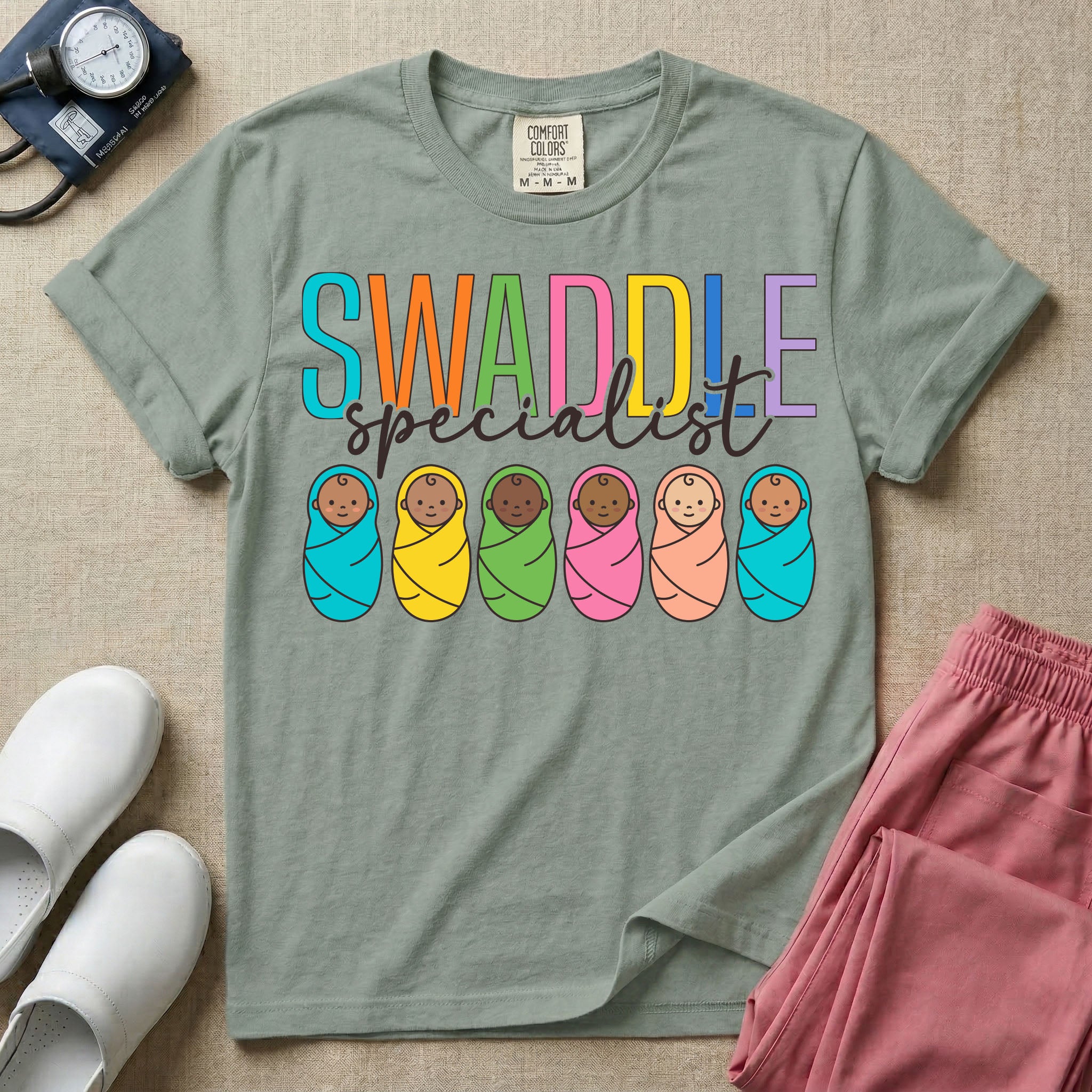 A cute neonatal and postpartum nurse graphic featuring the word SWADDLE in bright multicolored block letters above the word specialist in a white cursive font, positioned over a row of six diverse babies wrapped in brightly colored swaddles.