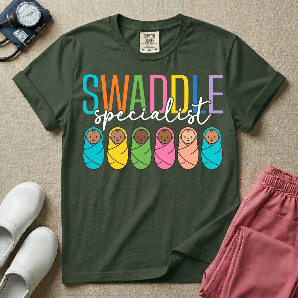 A cute neonatal and postpartum nurse graphic featuring the word SWADDLE in bright multicolored block letters above the word specialist in a white cursive font, positioned over a row of six diverse babies wrapped in brightly colored swaddles.