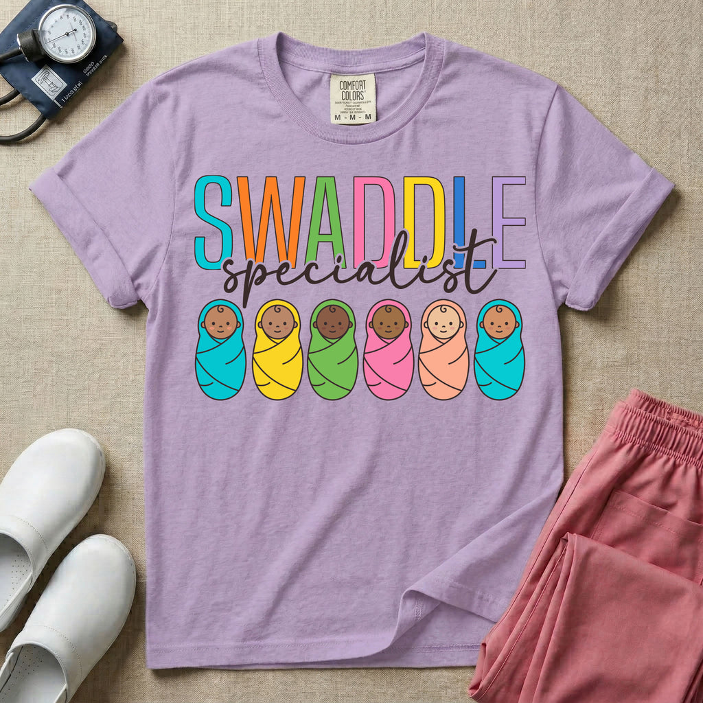 A cute neonatal and postpartum nurse graphic featuring the word SWADDLE in bright multicolored block letters above the word specialist in a white cursive font, positioned over a row of six diverse babies wrapped in brightly colored swaddles.