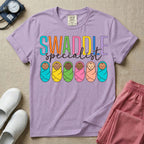 A cute neonatal and postpartum nurse graphic featuring the word SWADDLE in bright multicolored block letters above the word specialist in a white cursive font, positioned over a row of six diverse babies wrapped in brightly colored swaddles.