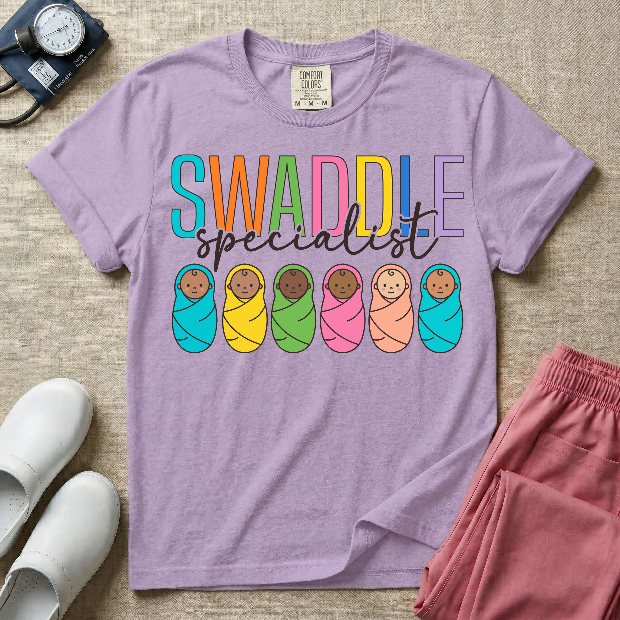 A cute neonatal and postpartum nurse graphic featuring the word SWADDLE in bright multicolored block letters above the word specialist in a white cursive font, positioned over a row of six diverse babies wrapped in brightly colored swaddles.