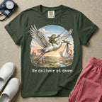 A humorous Labor and Delivery graphic featuring a storybook illustration of a frog dressed as a knight wielding a sword, riding on the back of a flying stork that is carrying a sleeping baby in a bundle, soaring over a fantasy landscape with a castle at sunrise, accompanied by text below that reads We deliver at dawn.