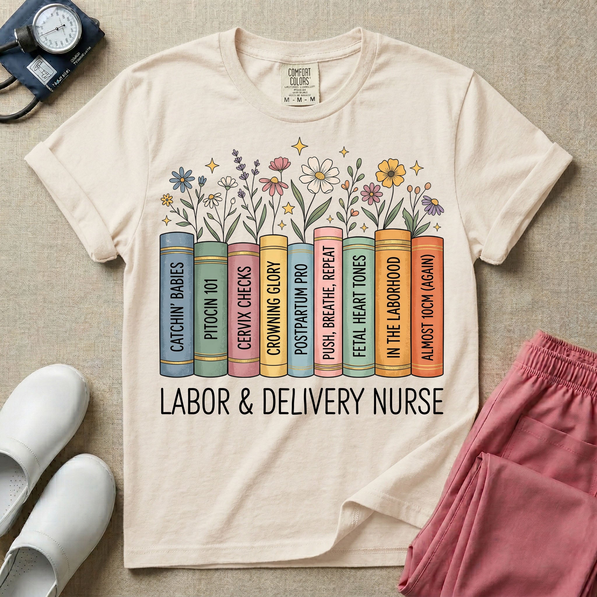 A Labor and Delivery nurse graphic featuring a row of standing books with colorful wildflowers blooming from the top pages. The book spines feature humorous titles reading CATCHIN' BABIES, PITOCIN 101, CERVIX CHECKS, CROWNING GLORY, POSTPARTUM PRO, PUSH, BREATHE, REPEAT, FETAL HEART TONES, IN THE LABORHOOD, and ALMOST 10CM (AGAIN), with the text LABOR & DELIVERY NURSE written directly below.