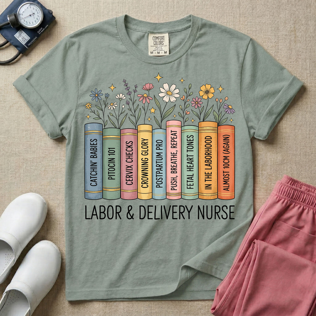 A Labor and Delivery nurse graphic featuring a row of standing books with colorful wildflowers blooming from the top pages. The book spines feature humorous titles reading CATCHIN' BABIES, PITOCIN 101, CERVIX CHECKS, CROWNING GLORY, POSTPARTUM PRO, PUSH, BREATHE, REPEAT, FETAL HEART TONES, IN THE LABORHOOD, and ALMOST 10CM (AGAIN), with the text LABOR & DELIVERY NURSE written directly below.