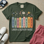 A Labor and Delivery nurse graphic featuring a row of standing books with colorful wildflowers blooming from the top pages. The book spines feature humorous titles reading CATCHIN' BABIES, PITOCIN 101, CERVIX CHECKS, CROWNING GLORY, POSTPARTUM PRO, PUSH, BREATHE, REPEAT, FETAL HEART TONES, IN THE LABORHOOD, and ALMOST 10CM (AGAIN), with the text LABOR & DELIVERY NURSE written directly below.