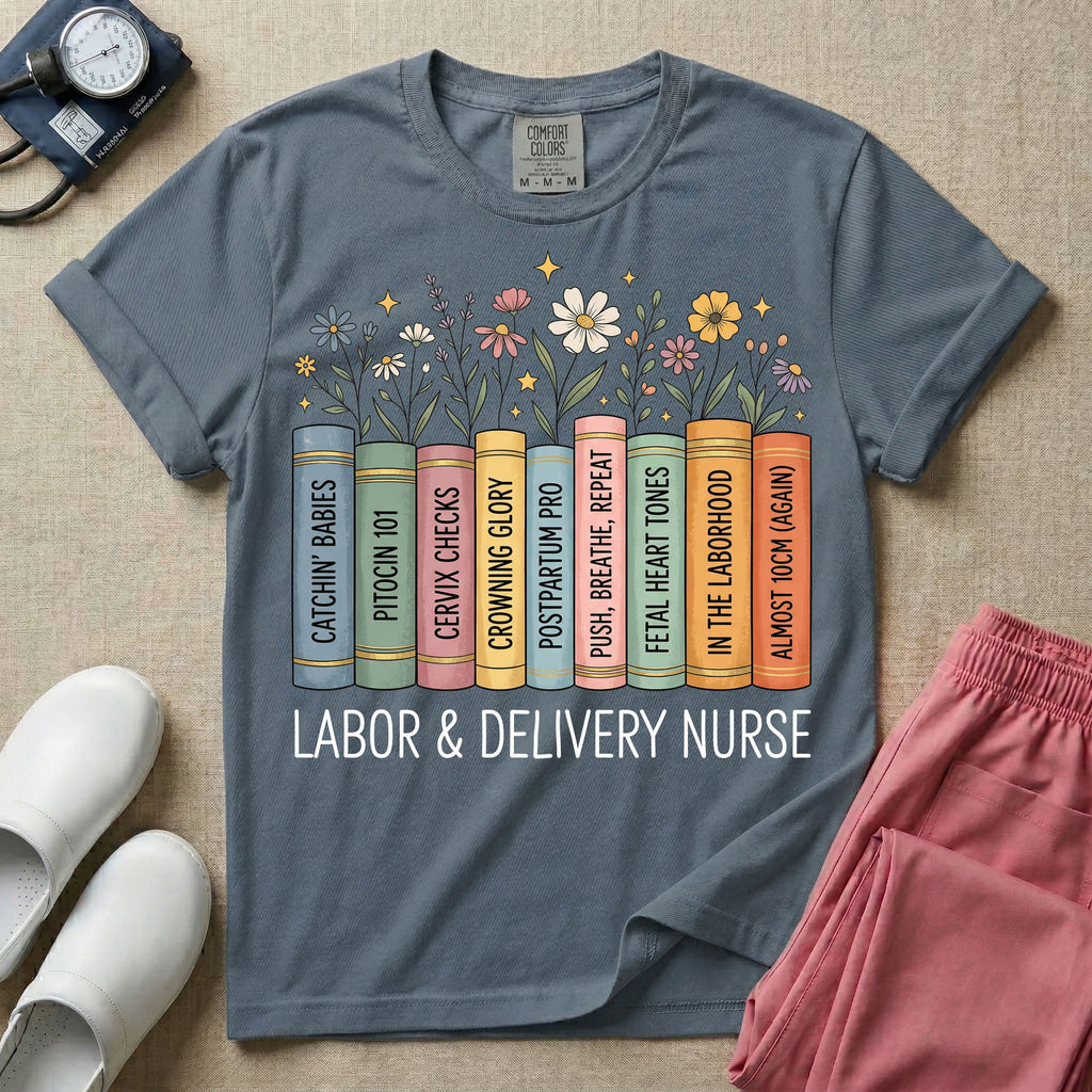 A Labor and Delivery nurse graphic featuring a row of standing books with colorful wildflowers blooming from the top pages. The book spines feature humorous titles reading CATCHIN' BABIES, PITOCIN 101, CERVIX CHECKS, CROWNING GLORY, POSTPARTUM PRO, PUSH, BREATHE, REPEAT, FETAL HEART TONES, IN THE LABORHOOD, and ALMOST 10CM (AGAIN), with the text LABOR & DELIVERY NURSE written directly below.