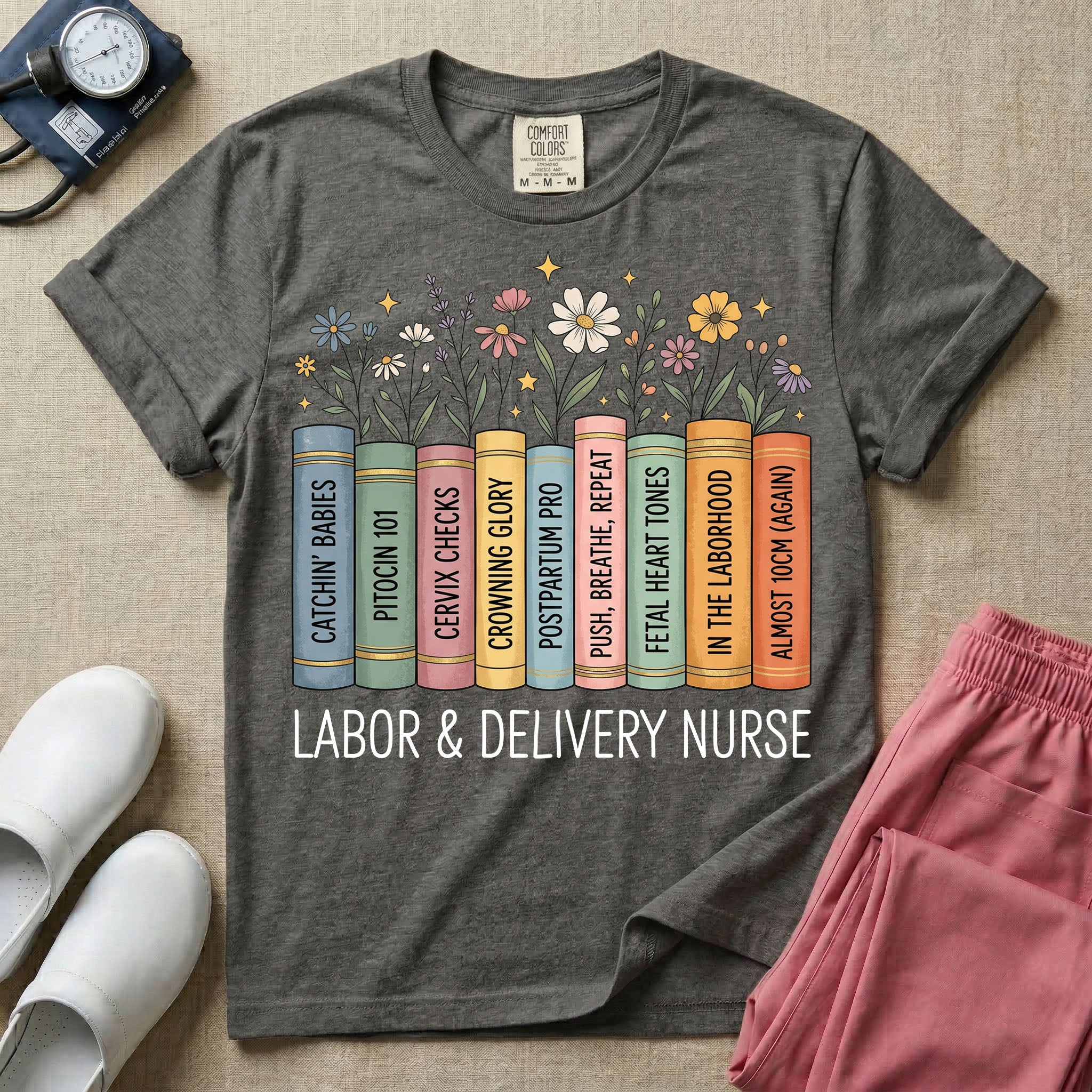 A Labor and Delivery nurse graphic featuring a row of standing books with colorful wildflowers blooming from the top pages. The book spines feature humorous titles reading CATCHIN' BABIES, PITOCIN 101, CERVIX CHECKS, CROWNING GLORY, POSTPARTUM PRO, PUSH, BREATHE, REPEAT, FETAL HEART TONES, IN THE LABORHOOD, and ALMOST 10CM (AGAIN), with the text LABOR & DELIVERY NURSE written directly below.