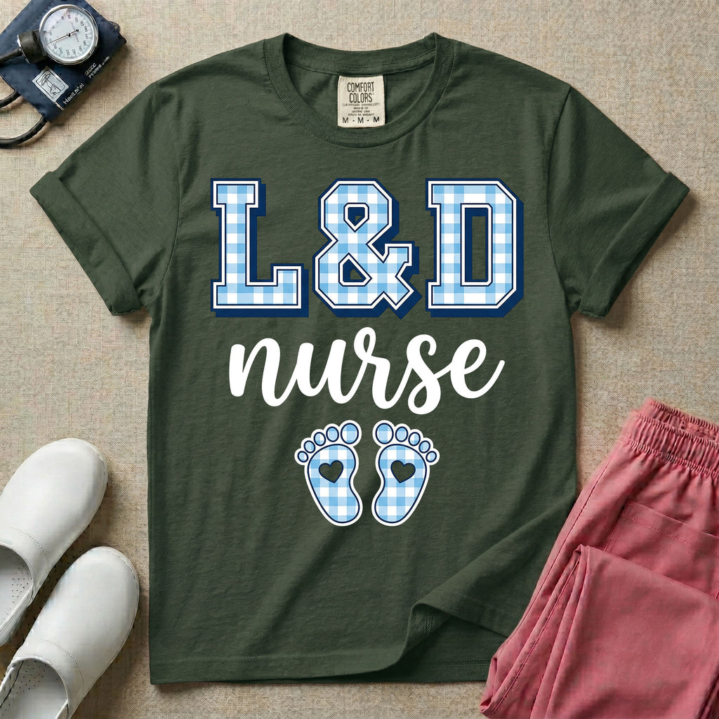 A graphic t-shirt for a Labor and Delivery unit featuring the text 'L&D nurse' with a light blue gingham pattern inside the block letters, along with matching blue gingham baby footprints featuring small heart cutouts.
