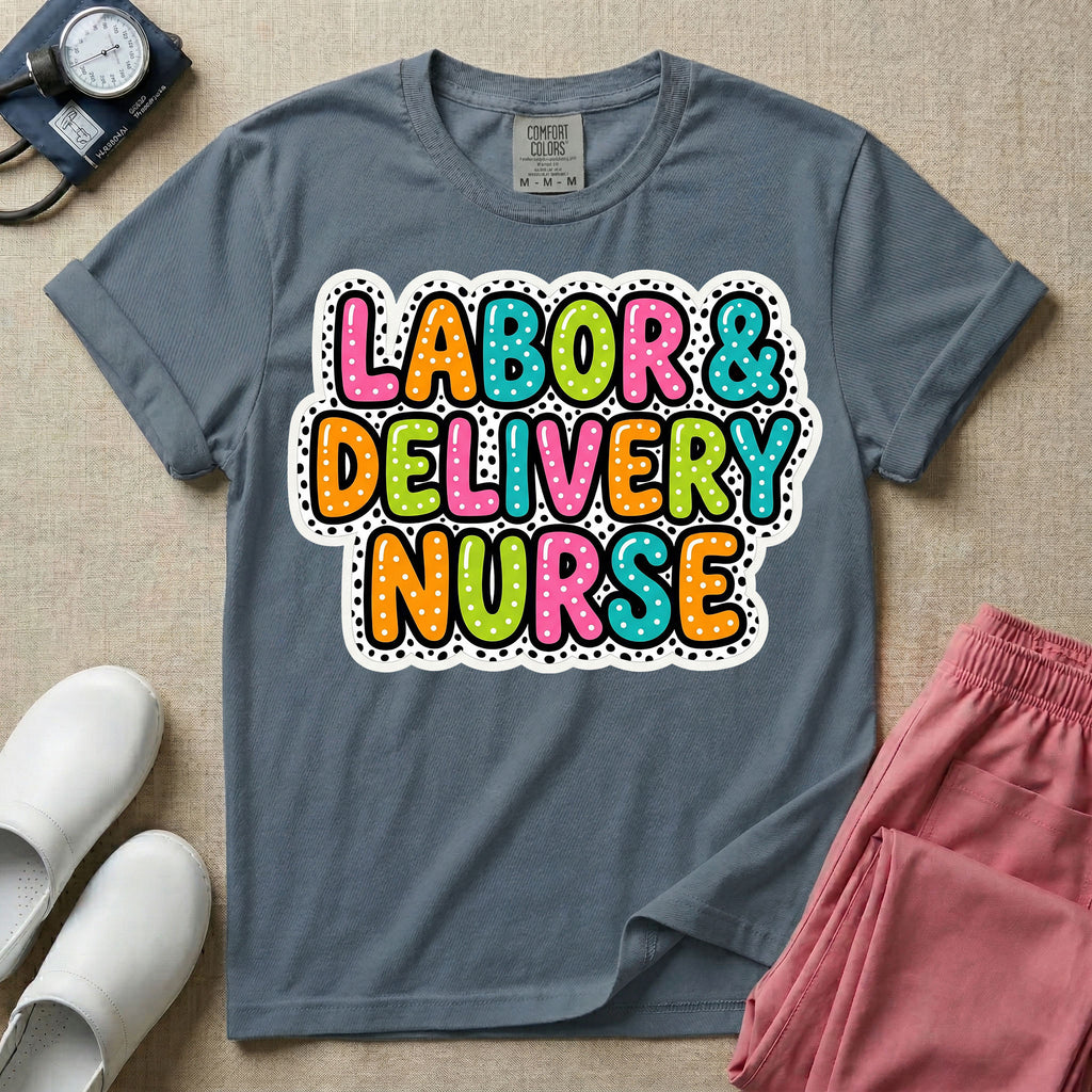 A graphic t-shirt for a Labor and Delivery unit featuring the text 'LABOR & DELIVERY NURSE' in bright, multicolored bubble lettering with white dots, framed by a contrasting black and white spotted background pattern.