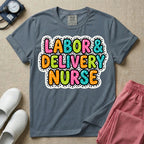 A graphic t-shirt for a Labor and Delivery unit featuring the text 'LABOR & DELIVERY NURSE' in bright, multicolored bubble lettering with white dots, framed by a contrasting black and white spotted background pattern.