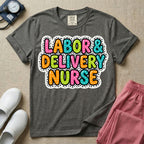 A graphic t-shirt for a Labor and Delivery unit featuring the text 'LABOR & DELIVERY NURSE' in bright, multicolored bubble lettering with white dots, framed by a contrasting black and white spotted background pattern.