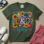 A colorful graphic t-shirt for a Labor and Delivery unit featuring the text "L&D" in leopard print, tie-dye, and cow print letters above the word "Nurse" in teal script, surrounded by detailed illustrations of sunflowers, a rainbow ultrasound gel bottle, a fetal monitor reading 145 bpm, a red stethoscope, and various hearts.