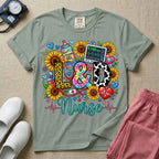 A colorful graphic t-shirt for a Labor and Delivery unit featuring the text "L&D" in leopard print, tie-dye, and cow print letters above the word "Nurse" in teal script, surrounded by detailed illustrations of sunflowers, a rainbow ultrasound gel bottle, a fetal monitor reading 145 bpm, a red stethoscope, and various hearts.