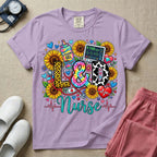 A colorful graphic t-shirt for a Labor and Delivery unit featuring the text "L&D" in leopard print, tie-dye, and cow print letters above the word "Nurse" in teal script, surrounded by detailed illustrations of sunflowers, a rainbow ultrasound gel bottle, a fetal monitor reading 145 bpm, a red stethoscope, and various hearts.