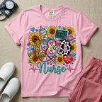 A colorful graphic t-shirt for a Labor and Delivery unit featuring the text "L&D" in leopard print, tie-dye, and cow print letters above the word "Nurse" in teal script, surrounded by detailed illustrations of sunflowers, a rainbow ultrasound gel bottle, a fetal monitor reading 145 bpm, a red stethoscope, and various hearts.