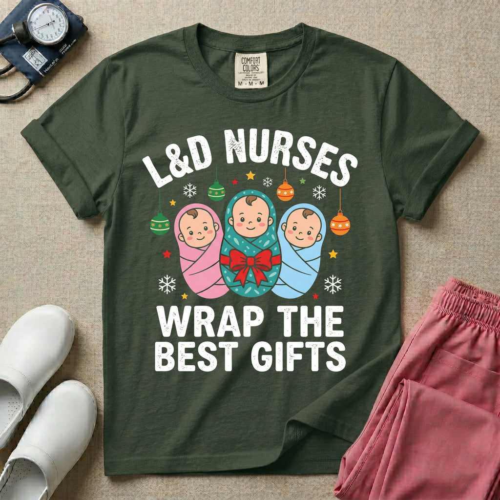 A festive Christmas graphic t-shirt for a Labor and Delivery unit featuring the funny text 'L&D NURSES WRAP THE BEST GIFTS' surrounding an illustration of three cute babies swaddled in pink, green with a red bow, and blue blankets, accented with holiday ornaments, snowflakes, and stars.