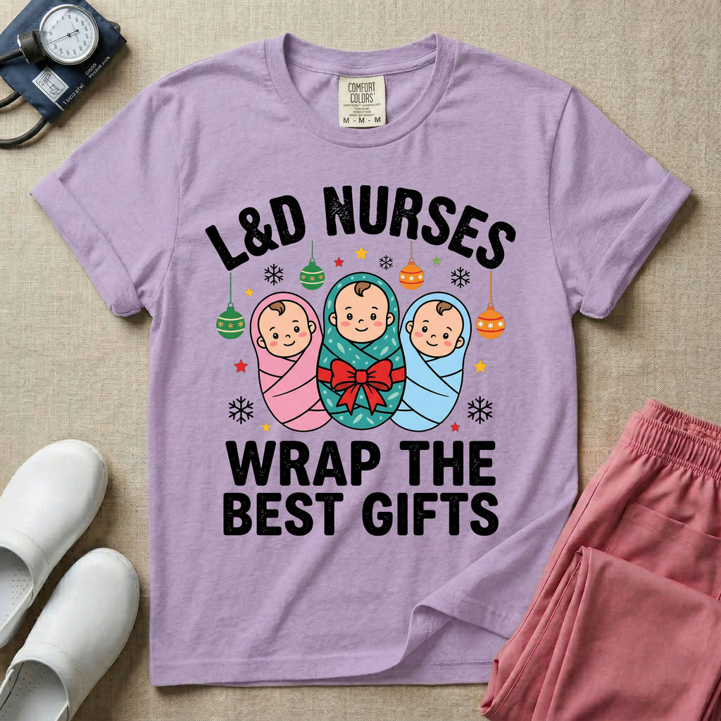 A festive Christmas graphic t-shirt for a Labor and Delivery unit featuring the funny text 'L&D NURSES WRAP THE BEST GIFTS' surrounding an illustration of three cute babies swaddled in pink, green with a red bow, and blue blankets, accented with holiday ornaments, snowflakes, and stars.