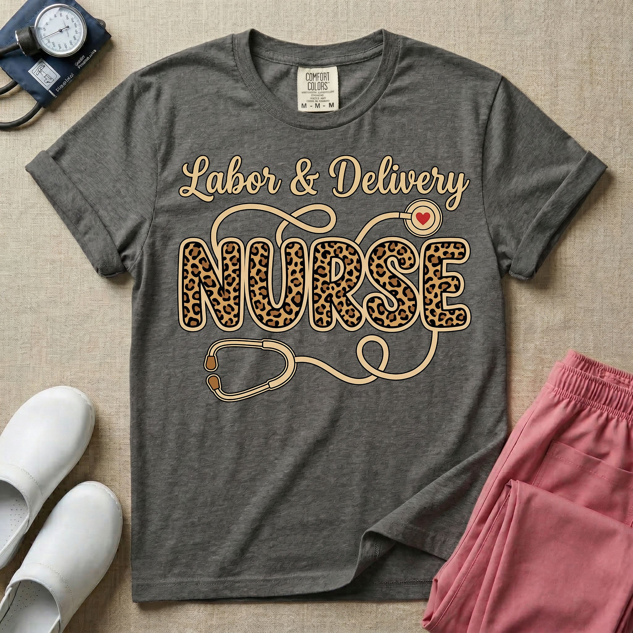 A graphic t-shirt for a Labor and Delivery unit featuring the text 'Labor & Delivery' in beige script above the word 'NURSE' in large leopard print letters, intertwined with an illustration of a stethoscope that features a small red heart on the chest piece.