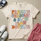 NICU nurse graphic featuring the phrase PREMIES SWADDLES & SLOW FLOW BOTTLES written in colorful retro wavy bubble letters.