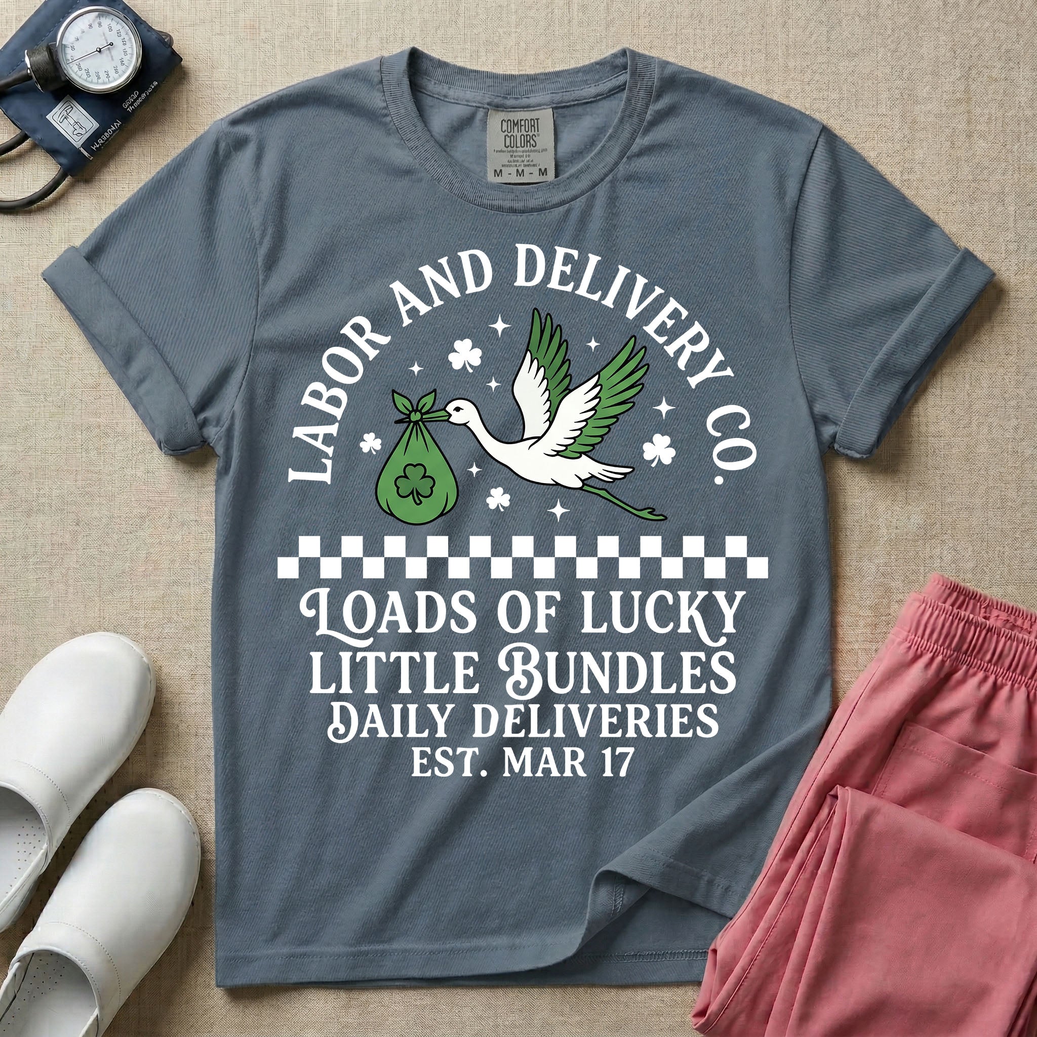 A retro Labor and Delivery nurse design featuring a flying stork carrying a sack with a shamrock, surrounded by stars and clovers, above a checkered border and the text "Labor and Delivery Co. Loads Of Lucky Little Bundles Daily Deliveries Est. Mar 17".