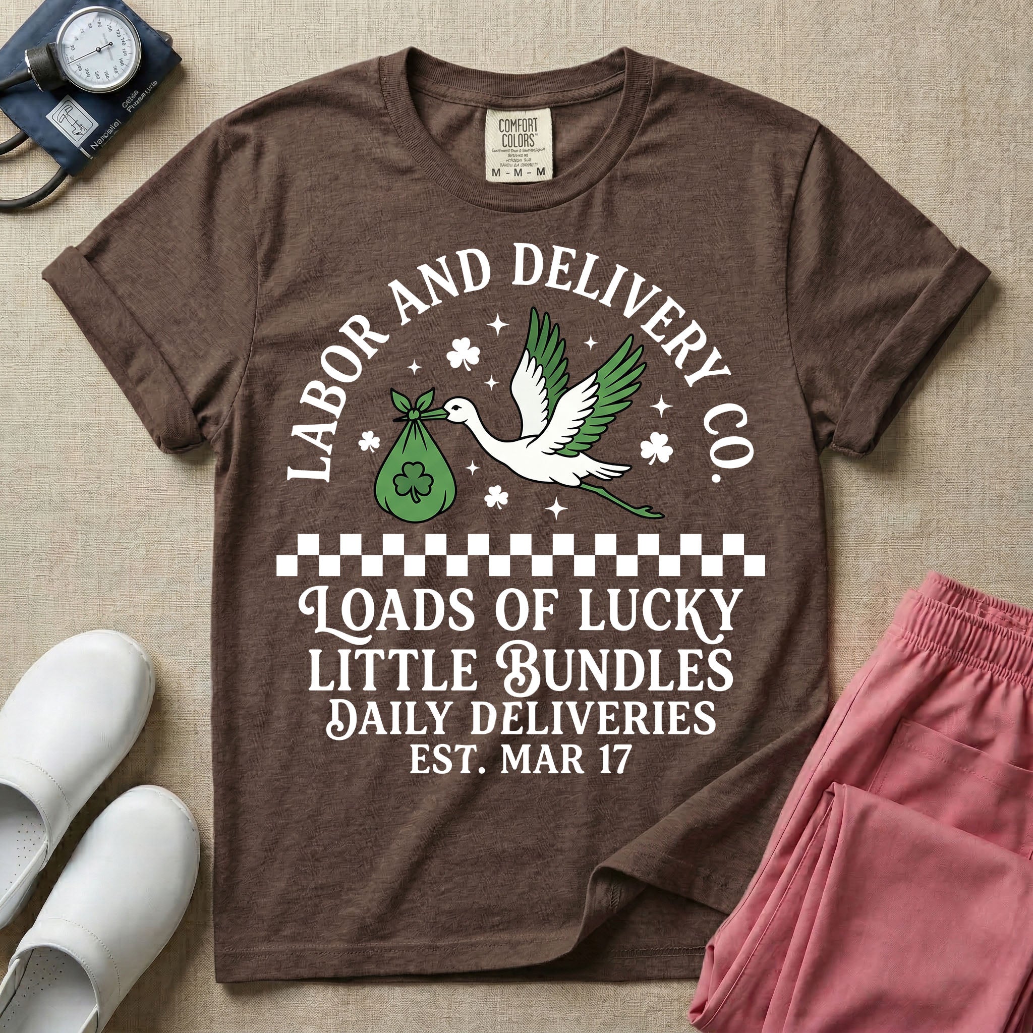 A retro Labor and Delivery nurse design featuring a flying stork carrying a sack with a shamrock, surrounded by stars and clovers, above a checkered border and the text "Labor and Delivery Co. Loads Of Lucky Little Bundles Daily Deliveries Est. Mar 17".