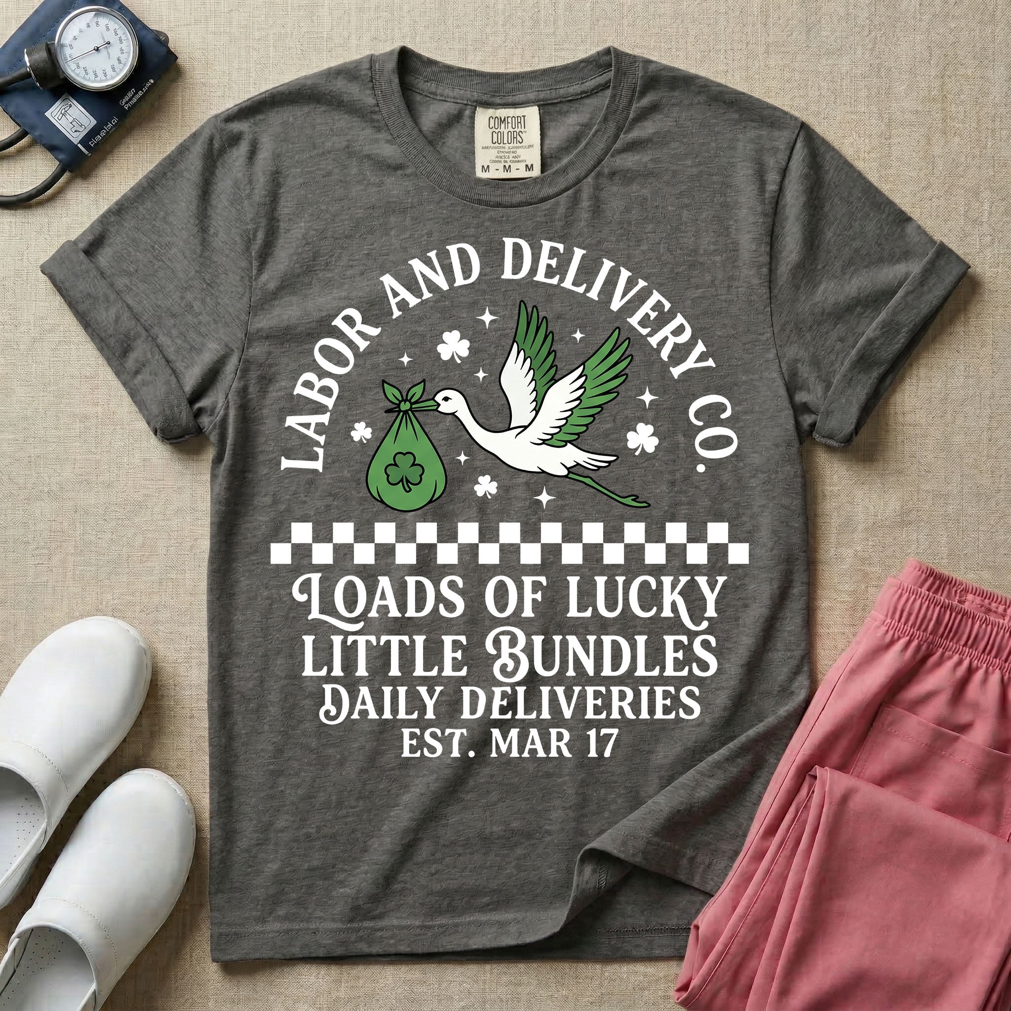 A retro Labor and Delivery nurse design featuring a flying stork carrying a sack with a shamrock, surrounded by stars and clovers, above a checkered border and the text "Labor and Delivery Co. Loads Of Lucky Little Bundles Daily Deliveries Est. Mar 17".