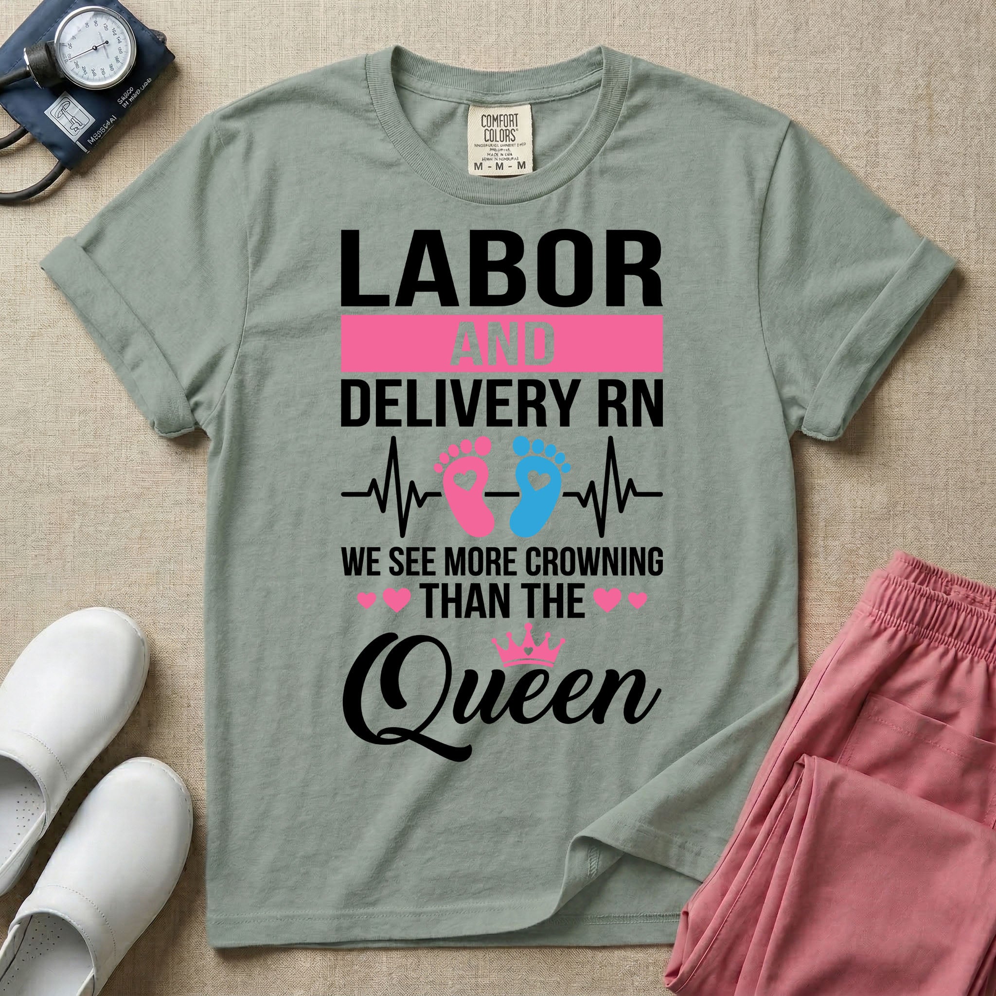 A humorous Labor and Delivery RN design featuring an EKG heartbeat line with pink and blue baby footprints, tiny pink hearts, a pink crown, and the text "LABOR AND DELIVERY RN WE SEE MORE CROWNING THAN THE Queen".