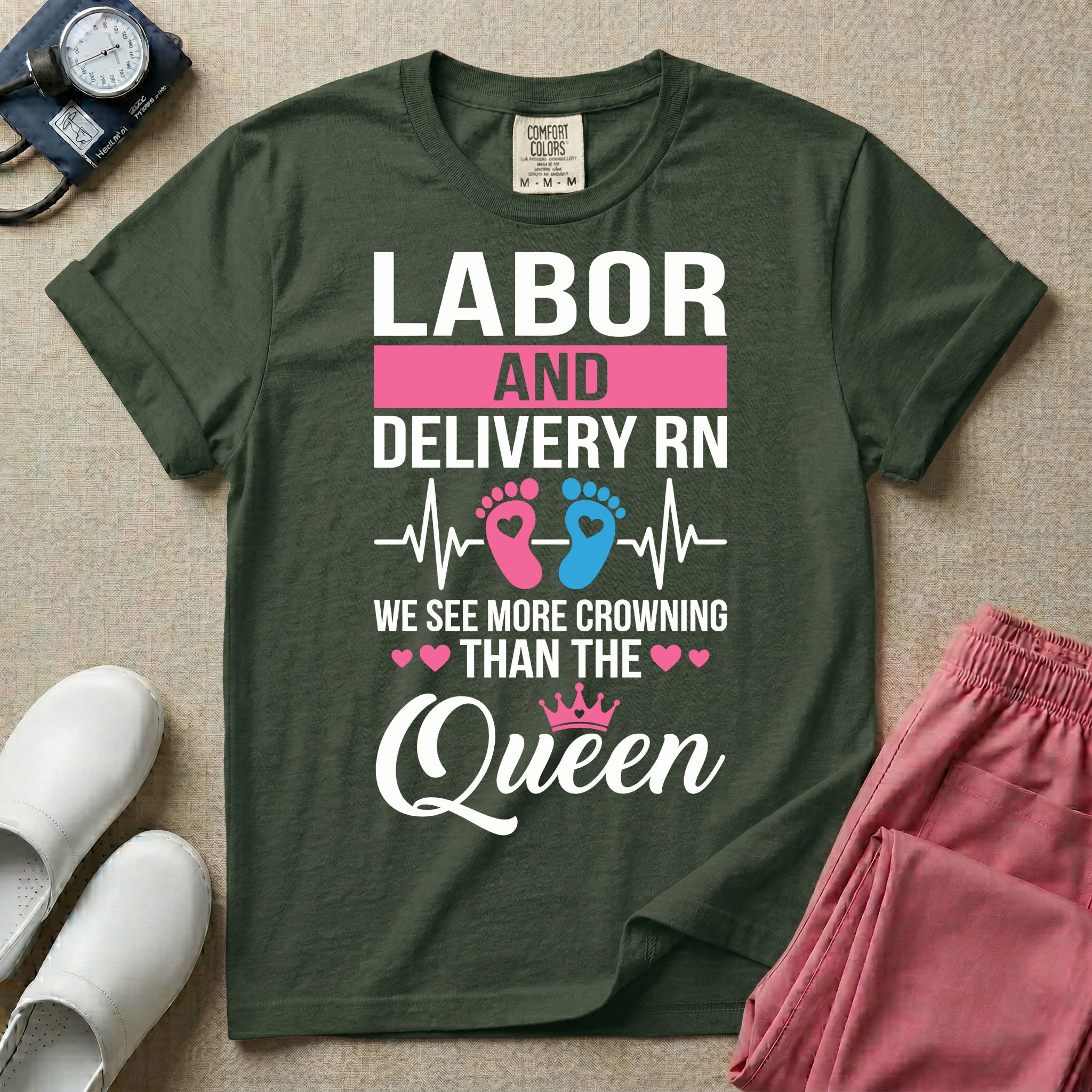 A humorous Labor and Delivery RN design featuring an EKG heartbeat line with pink and blue baby footprints, tiny pink hearts, a pink crown, and the text "LABOR AND DELIVERY RN WE SEE MORE CROWNING THAN THE Queen".