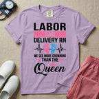 A humorous Labor and Delivery RN design featuring an EKG heartbeat line with pink and blue baby footprints, tiny pink hearts, a pink crown, and the text "LABOR AND DELIVERY RN WE SEE MORE CROWNING THAN THE Queen".