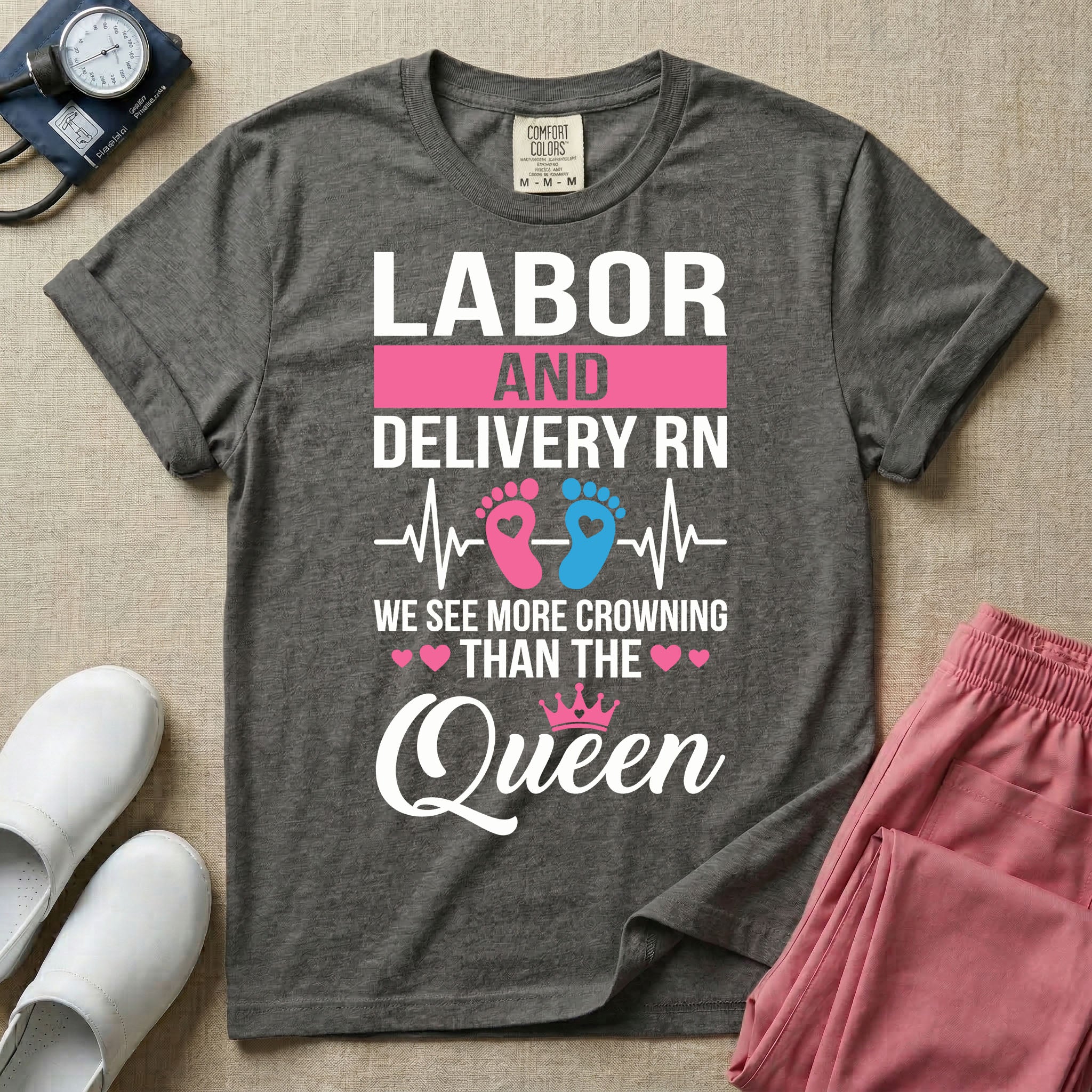 A humorous Labor and Delivery RN design featuring an EKG heartbeat line with pink and blue baby footprints, tiny pink hearts, a pink crown, and the text "LABOR AND DELIVERY RN WE SEE MORE CROWNING THAN THE Queen".