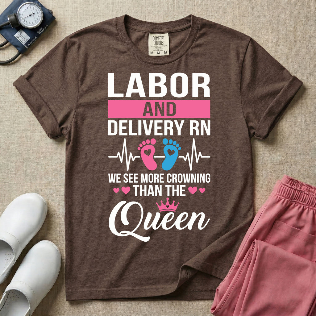 A humorous Labor and Delivery RN design featuring an EKG heartbeat line with pink and blue baby footprints, tiny pink hearts, a pink crown, and the text "LABOR AND DELIVERY RN WE SEE MORE CROWNING THAN THE Queen".