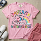 A cute Labor and Delivery and Midwife design featuring a heart-shaped stethoscope enclosing pink and blue baby footprints next to a pastel rainbow and small stars, accompanied by the text "PATIENTLY WAITING FOR 10 CM" in colorful lettering.