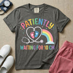 A cute Labor and Delivery and Midwife design featuring a heart-shaped stethoscope enclosing pink and blue baby footprints next to a pastel rainbow and small stars, accompanied by the text "PATIENTLY WAITING FOR 10 CM" in colorful lettering.