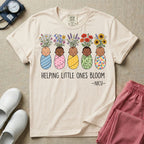 A Neonatal Intensive Care Unit nurse design featuring five peacefully sleeping, diverse babies in differently patterned swaddles with vibrant flowers like sunflowers and daisies blooming from the tops of their heads, positioned above the text "HELPING LITTLE ONES BLOOM -NICU-".