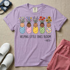 A Neonatal Intensive Care Unit nurse design featuring five peacefully sleeping, diverse babies in differently patterned swaddles with vibrant flowers like sunflowers and daisies blooming from the tops of their heads, positioned above the text "HELPING LITTLE ONES BLOOM -NICU-".