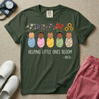 A Neonatal Intensive Care Unit nurse design featuring five peacefully sleeping, diverse babies in differently patterned swaddles with vibrant flowers like sunflowers and daisies blooming from the tops of their heads, positioned above the text "HELPING LITTLE ONES BLOOM -NICU-".