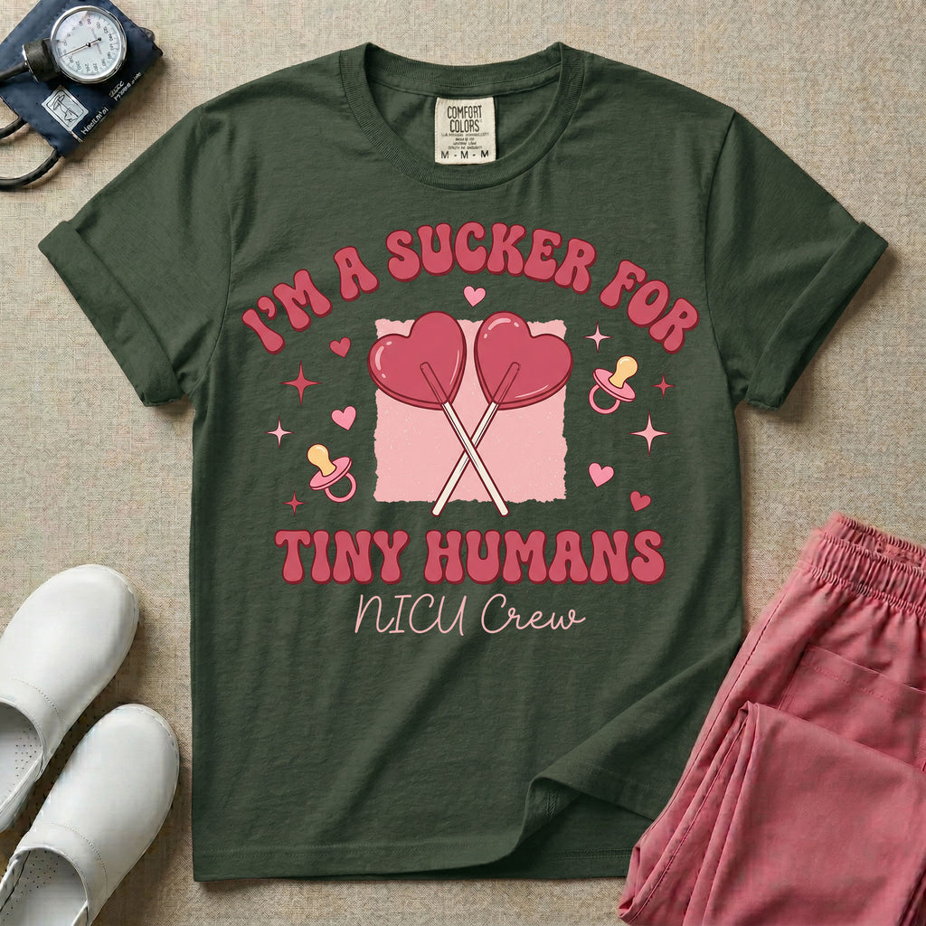 A retro Neonatal Intensive Care Unit nurse design featuring two crossed heart-shaped lollipops over a textured pink square, flanked by two baby pacifiers, sparkling stars, and small hearts, surrounded by the humorous text "I'M A SUCKER FOR TINY HUMANS NICU Crew" in a red and pink groovy font.