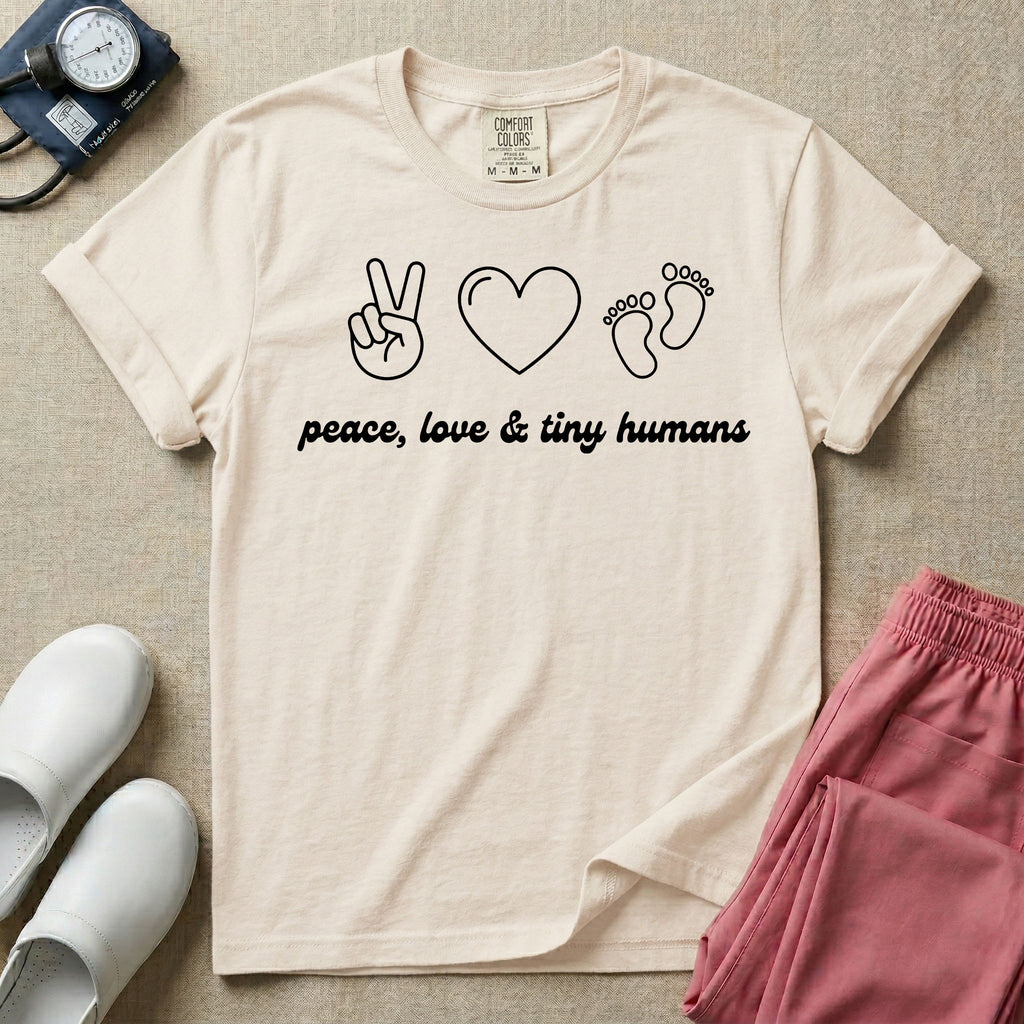 A t-shirt featuring minimalist line art of a peace sign, a heart, and baby footprints above the text "peace, love & tiny humans" designed for NICU, labor and delivery, and pediatric nurses.