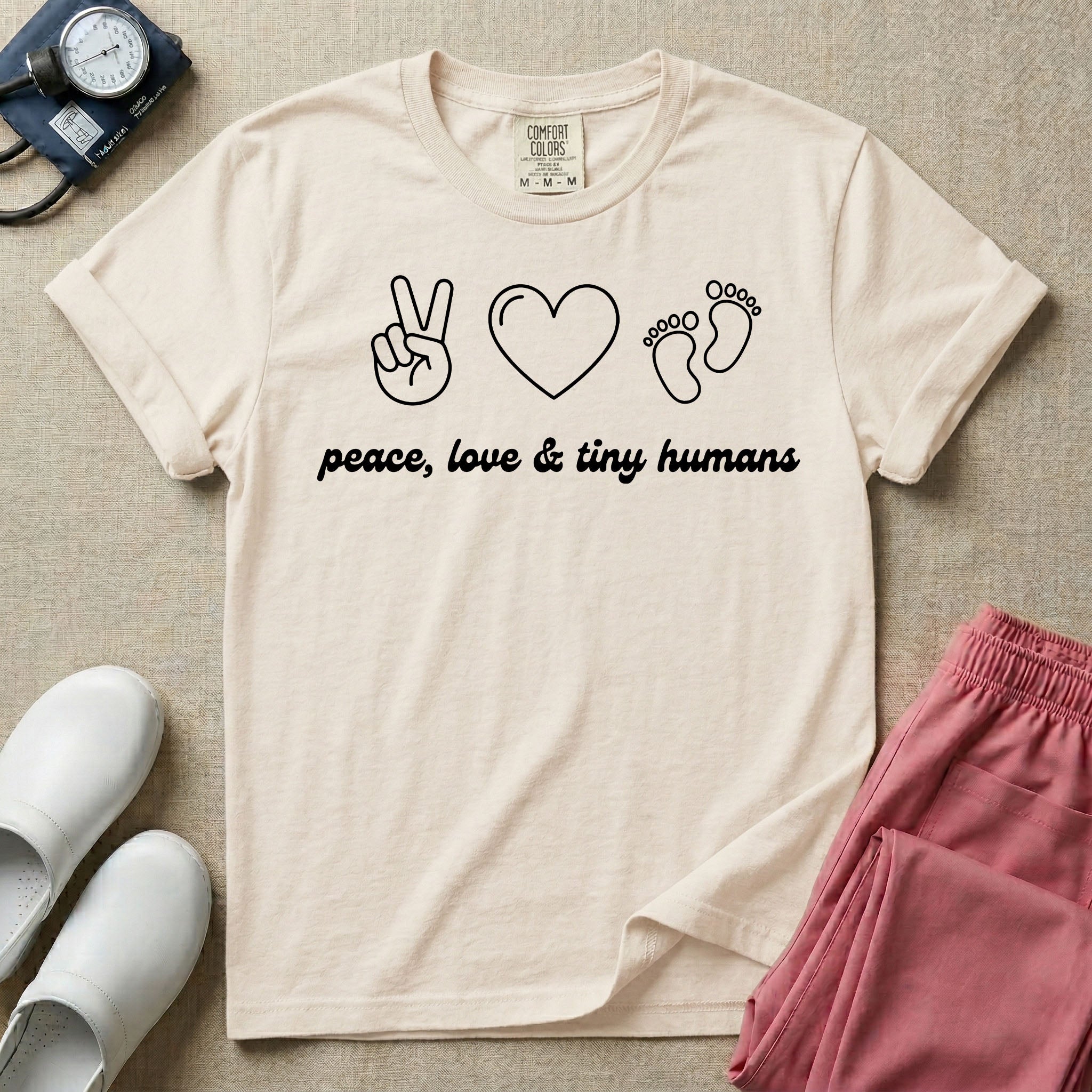 A t-shirt featuring minimalist line art of a peace sign, a heart, and baby footprints above the text "peace, love & tiny humans" designed for NICU, labor and delivery, and pediatric nurses.