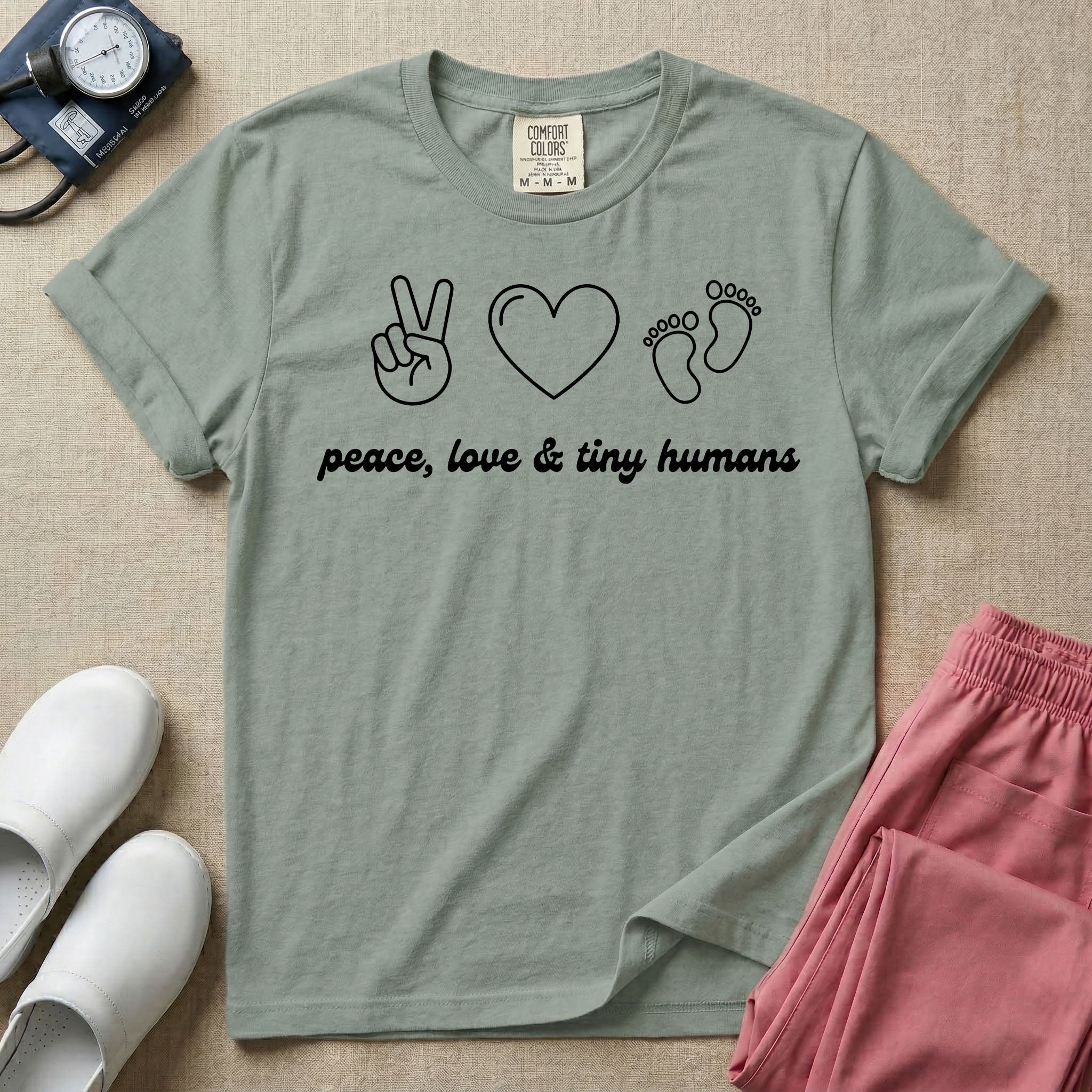 A t-shirt featuring minimalist line art of a peace sign, a heart, and baby footprints above the text "peace, love & tiny humans" designed for NICU, labor and delivery, and pediatric nurses.