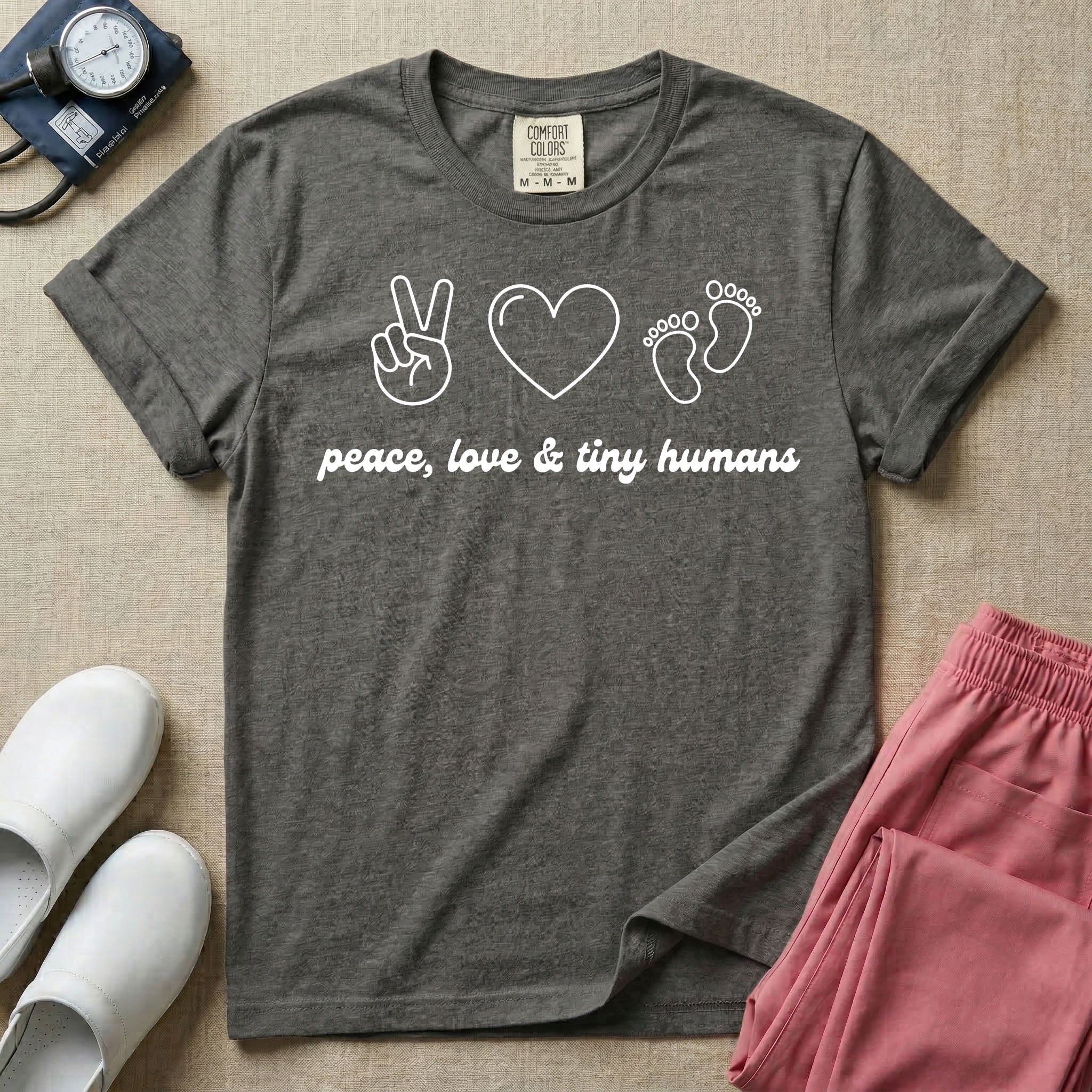A t-shirt featuring minimalist line art of a peace sign, a heart, and baby footprints above the text "peace, love & tiny humans" designed for NICU, labor and delivery, and pediatric nurses.
