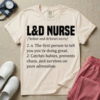 A graphic featuring a dictionary definition style layout with the bold heading L&D NURSE, followed by the phonetic pronunciation and two humorous definitions reading "1. n. The first person to tell you you're doing great." and "2. Catches babies, prevents chaos, and survives on pure adrenaline." in white text, designed for labor and delivery nurses.