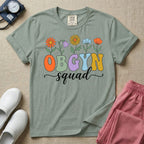 A retro floral graphic design for an OB-GYN unit featuring colorful retro flowers growing out of the letters OBGYN, with the word squad written below in a white cursive script.