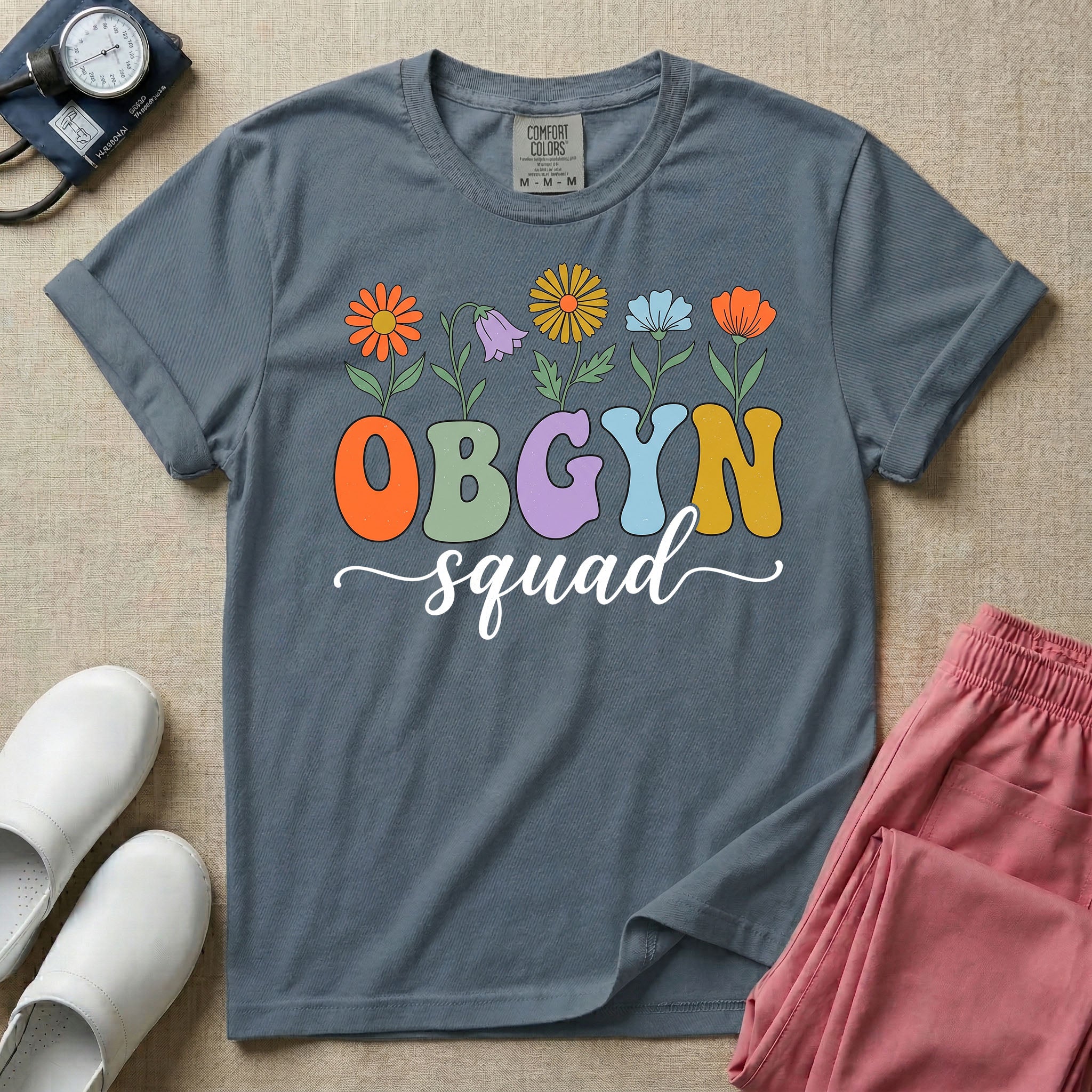 A retro floral graphic design for an OB-GYN unit featuring colorful retro flowers growing out of the letters OBGYN, with the word squad written below in a white cursive script.